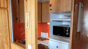 Una cucina compatta con mobili in legno, un forno a microonde e un frigorifero bianco.