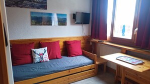 Una stanza accogliente con un divano in legno, cuscini rossi, un tavolino di legno e una finestra con tende.