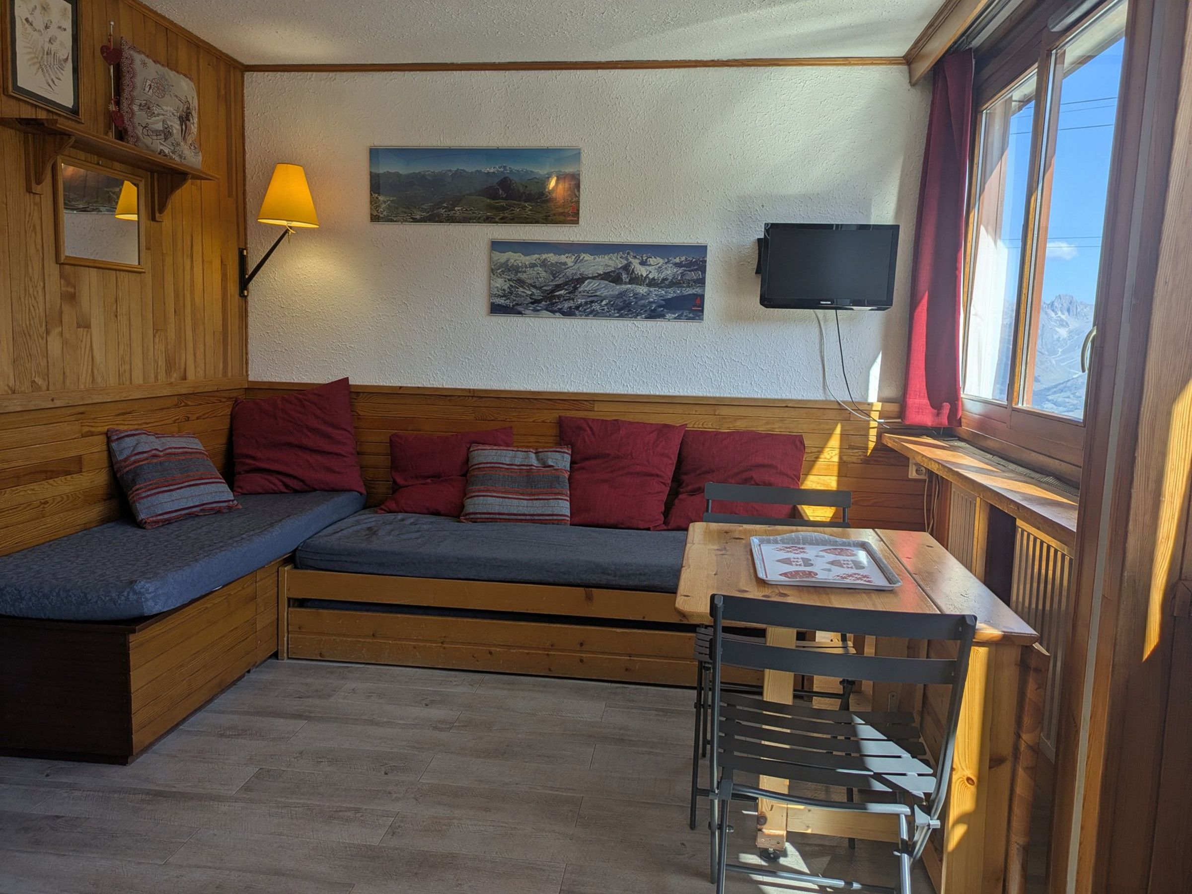 A cozy room with a wooden bench, a table, and chairs, a wall-mounted TV, and framed pictures.