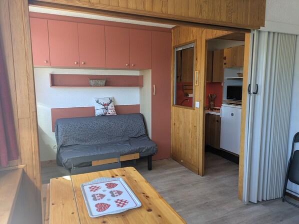 Ein gemütlicher Wohnbereich mit einer Couch, einem Tisch mit dekorativem Teller und einer kleinen Küche im Hintergrund.
