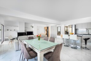 A modern kitchen with stainless steel appliances, a dining area with a glass table, and a living space with a sofa and chairs.