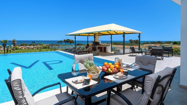 A poolside dining area with a table set for two, a fruit bowl, and a view of the ocean.