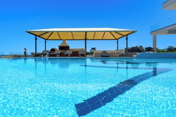 A clear swimming pool with lounge chairs and a covered seating area.