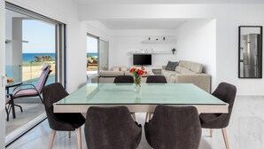 A modern dining area with a glass table, dark chairs, and a view of the sea.