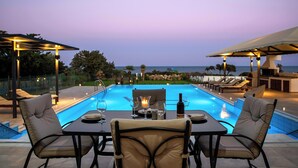 An outdoor pool area with lounge chairs, a table set for dining, and a view of the ocean at dusk.