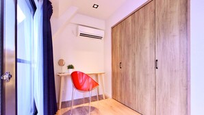 Une pièce avec un plancher en bois, une chaise rouge, un bureau avec une petite plante et une grande armoire en bois.