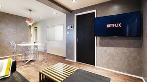 Una habitación moderna con un televisor de pantalla plana mostrando 'NETFLIX', una mesa de centro de madera y una zona de estar con un banco y sillas.