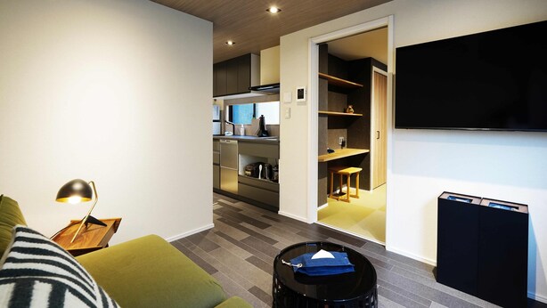 A modern living room with a sofa, a lamp, and a black coffee table. There is a kitchen area visible in the background. - Real Life SANGENJAYA 1BR  2Pax Shibuya (Meguro)