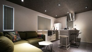 A modern living room with a sofa, a small table, and a kitchen area with a microwave and bar stools. - Real Life AOYAMA 2BR suite 5pax 3bed 3min metro (Minato)
