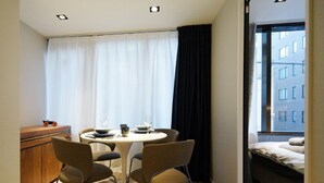A compact dining area with a round table and four chairs, a small wooden cabinet, and a window with curtains.