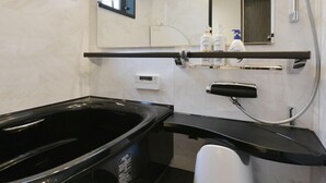 A modern bathroom with a black bathtub, a mirror, and a shower head.