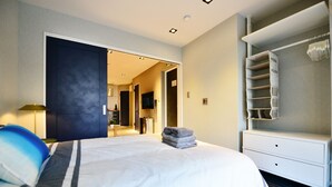 A modern hotel room with a large bed, a walk-in closet, and a bathroom visible through an open door.