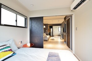 Une chambre d’hôtel moderne dotée d’un grand lit, d’une table de chevet, d’une télévision et offrant une vue sur le couloir et l’espace cuisine.