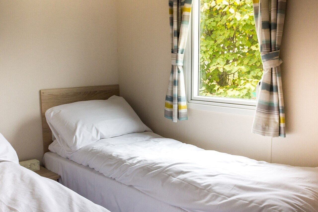 A single bed with white bedding in a room with a window.