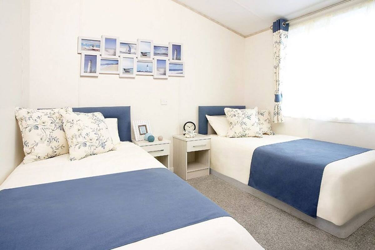 Un dormitorio con dos camas, una mesita de noche, un escritorio y una ventana con cortinas.