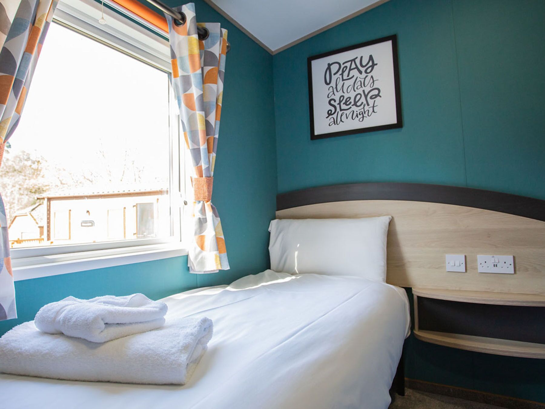 Une chambre d’hôtel avec un lit, une fenêtre avec des rideaux, un mur orné d’une citation encadrée et une tête de lit.