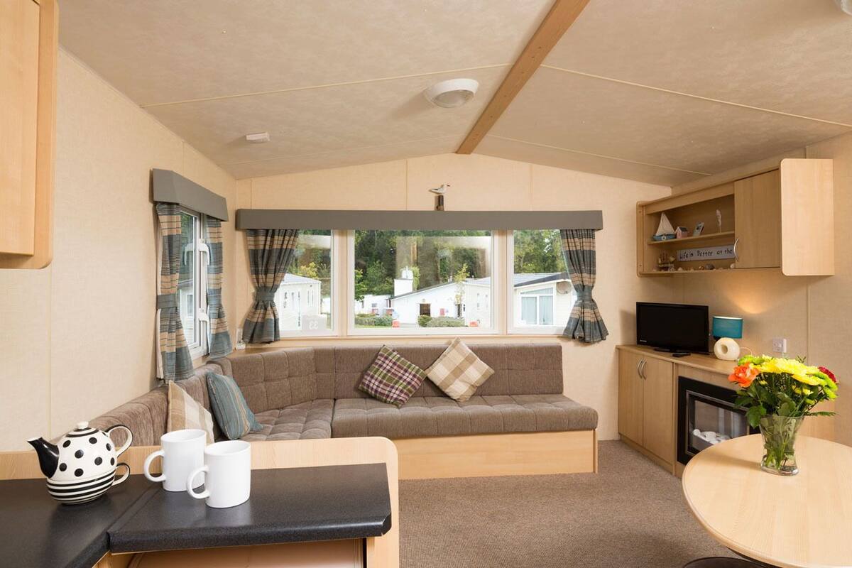 Una sala acogedora con sofá, una mesita, televisor y ventana con cortinas.