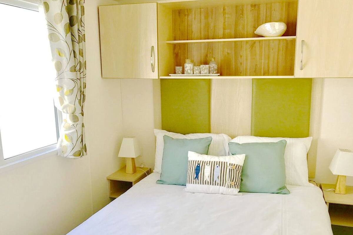 Un dormitorio con una cama, dos mesitas de noche, una mesilla auxiliar, un cabecero de madera y un estante con adornos.