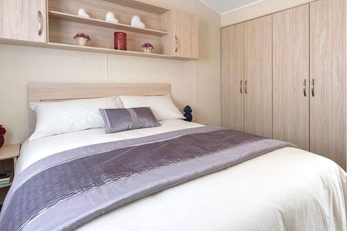 Un dormitorio con cama, mesita de noche, estante con objetos decorativos y armario.
