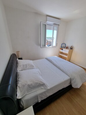 A bedroom with a bed, a wooden dresser, and a window with a view of buildings.