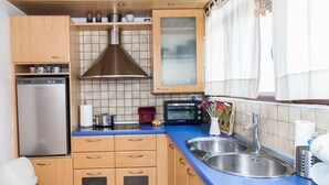 Cocina compacta con armarios de madera, pileta de acero inoxidable, tostadora y refrigerador.