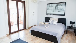 Un dormitorio con una cama, una mesita de noche con lámpara, un cuadro en la pared y un ventanal corredero que da a un espacio exterior.