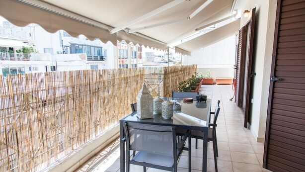 Un balcón con mesa y sillas, un cerramiento de bambú y vistas a edificios.
