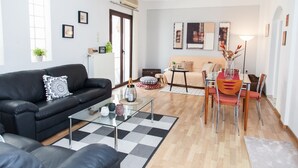 Una sala moderna con un sofá de cuero negro, una mesa de centro de vidrio y un comedor con mesa y sillas de madera.