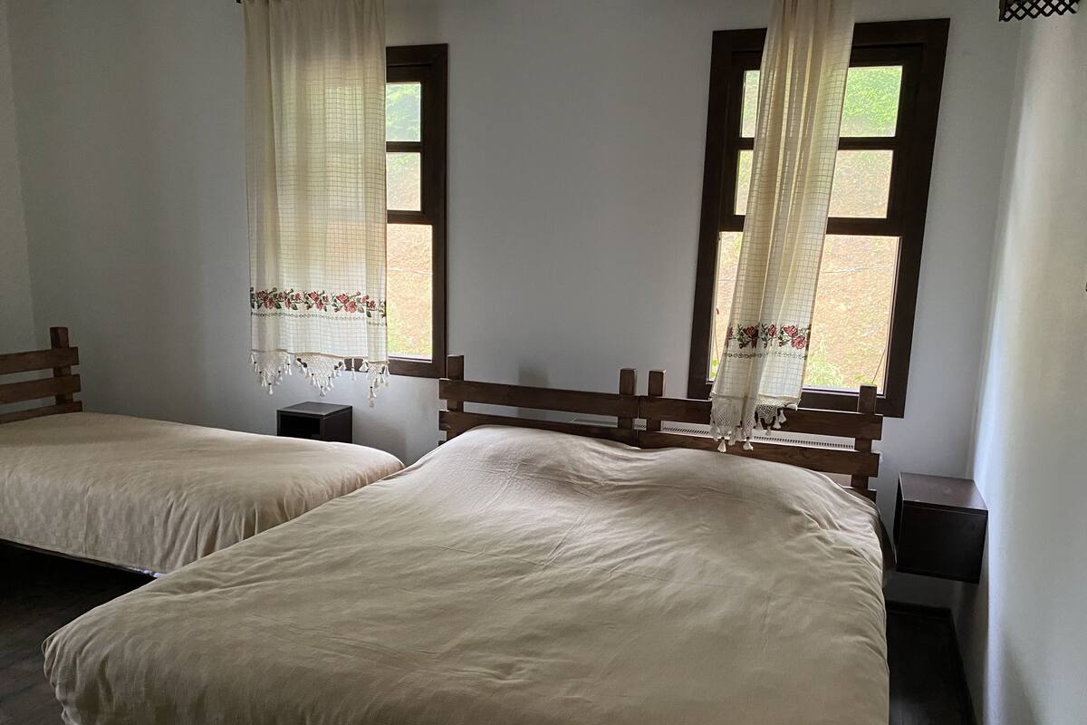 Une chambre avec deux lits simples, des têtes de lit en bois, une petite table de chevet et une fenêtre donnant sur un paysage verdoyant.