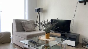 Moderni olohuone, jossa on lasinen sohvapöytä, sohva, televisio ja lattiavalaisin.