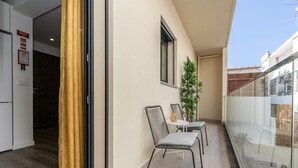 Een balkon met een glazen hekwerk, een kleine tafel met twee stoelen en een bloempot met een plant.