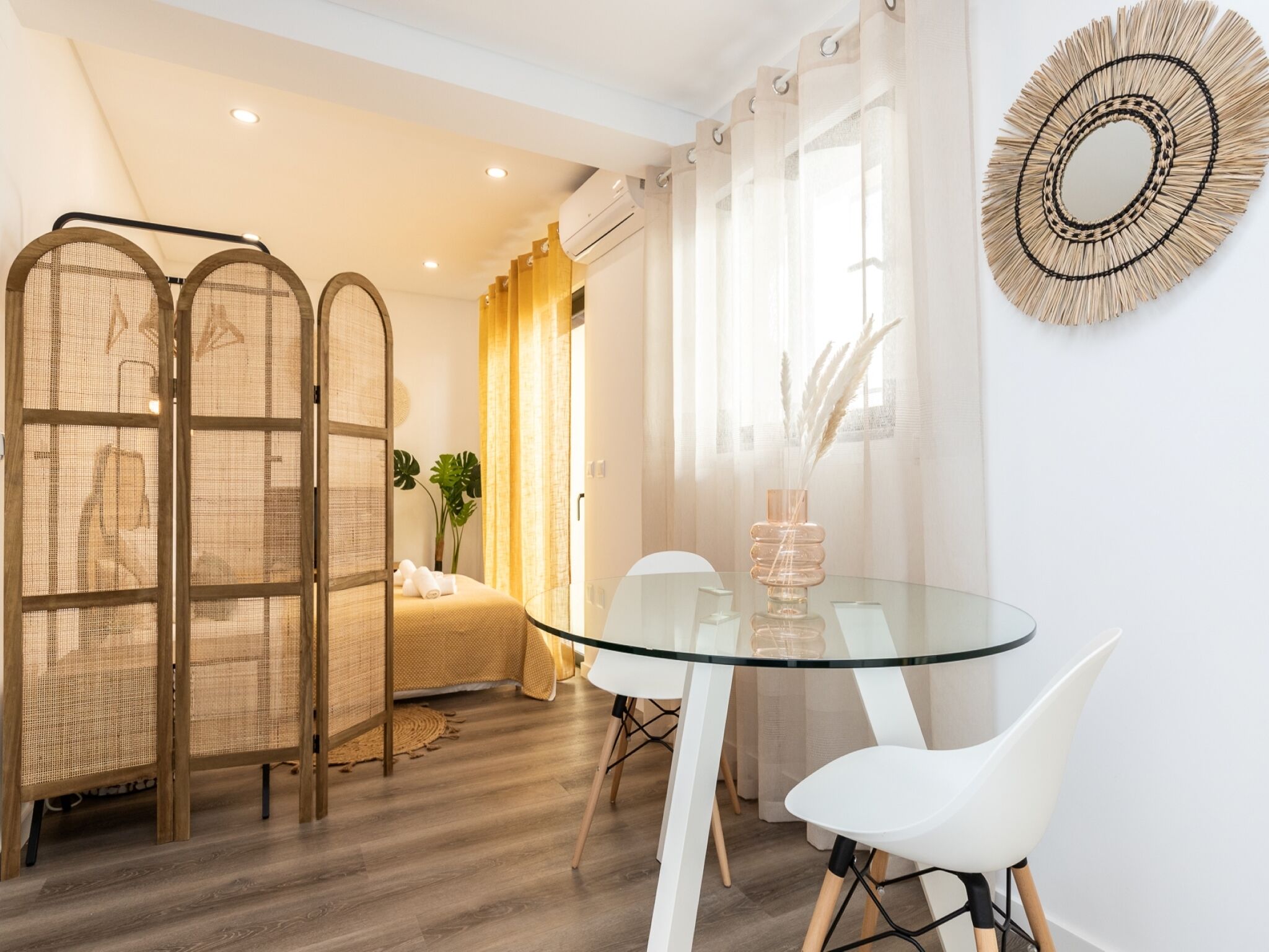 Un dormitorio moderno con una mesita de vidrio, sillas blancas y una cama con cabecero.