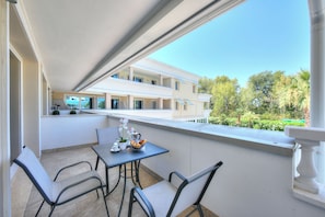 A balcony with a table and chairs, a potted plant, and a view of a building and greenery. - Rivoltella Apt With Pool 600m From Lake (Desenzano del Garda)