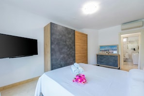 A modern hotel room with a flat-screen TV, a bed with white linens, a wooden accent wall, and a painting on the dresser. - Rivoltella Apt With Pool 600m From Lake (Desenzano del Garda)