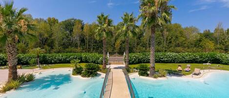 Una amplia piscina exterior con un paseo central, rodeada de palmeras y follaje.