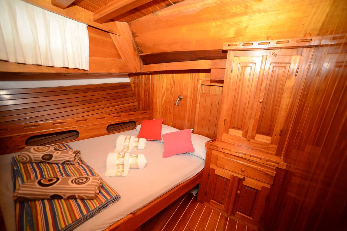 A wooden cabin interior with a bed, pillows, and a small wooden cabinet.
