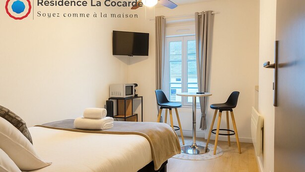 A hotel room with a bed, a TV, a microwave, two chairs, and a small table. - Résidence La Cocarde (Bourges)