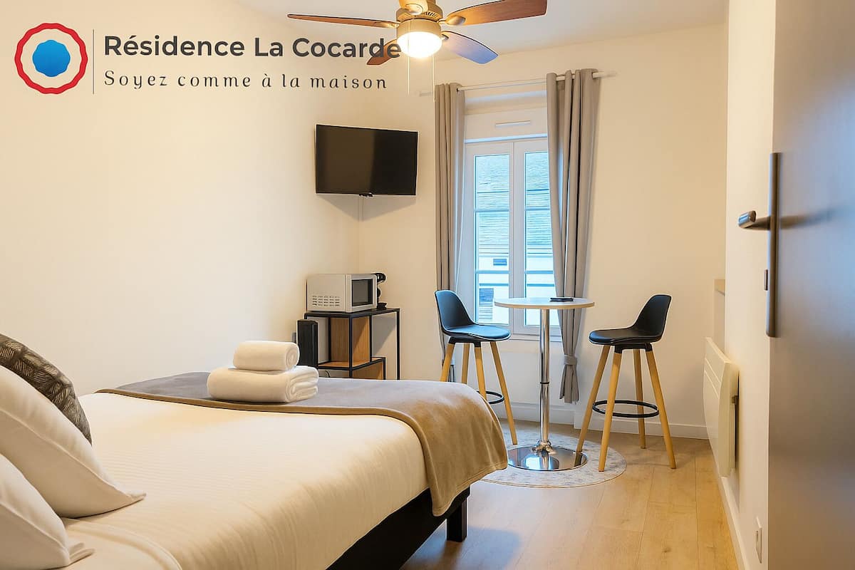 A hotel room with a bed, a TV, a microwave, two chairs, and a small table.