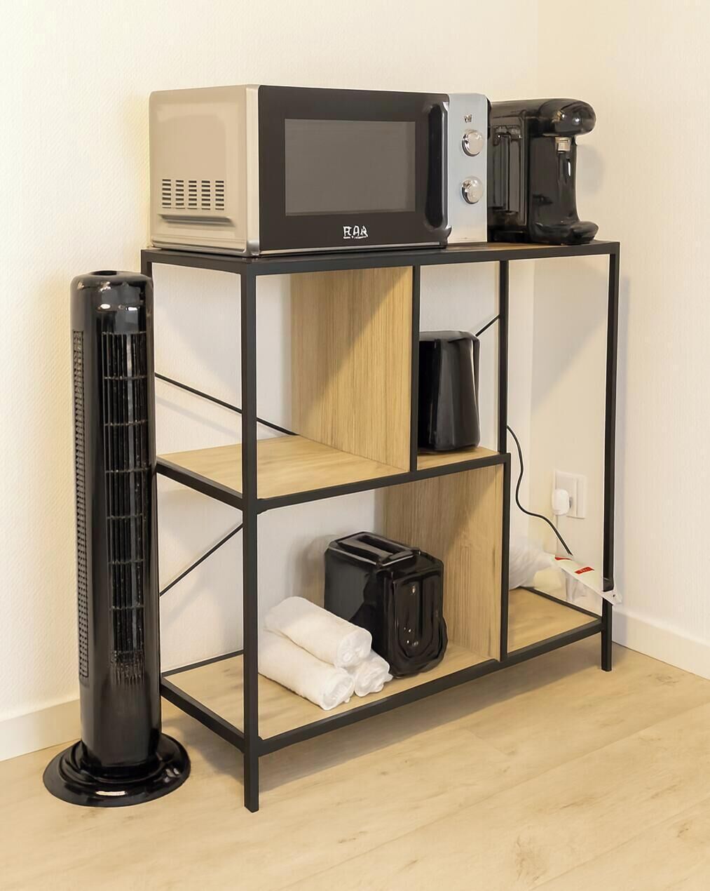 A compact kitchenette with a microwave, toaster, and coffee maker on a black metal stand.