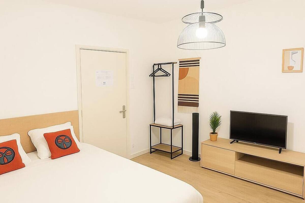 A hotel room with a bed, a TV, a hanging light fixture, and a coat rack.