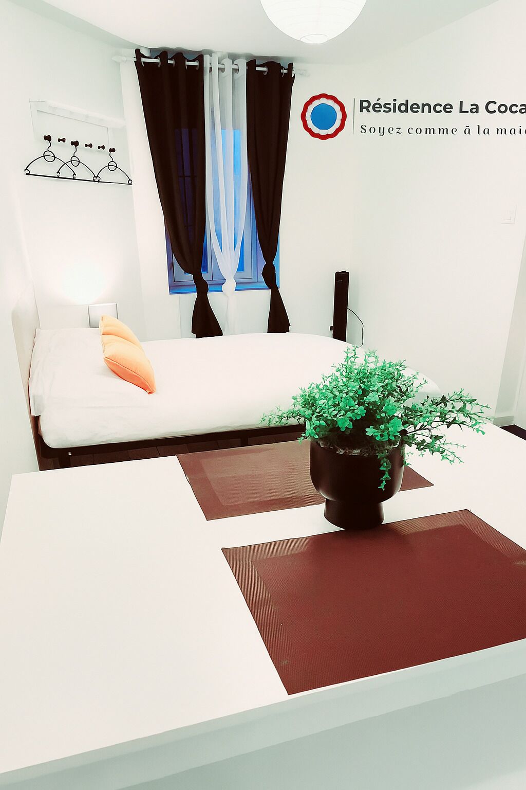 Ein modernes Schlafzimmer mit einem Bett, einem Nachttisch mit Pflanze und einem Fenster mit Vorhängen.