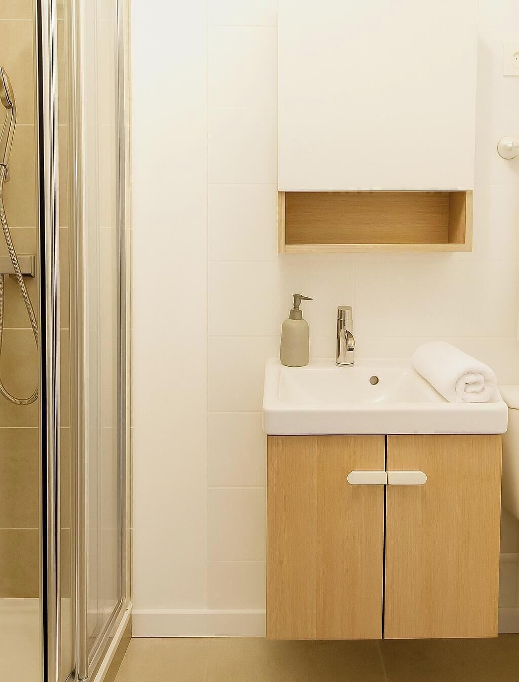 Een badkamer met een glazen douchecabine, een witte wastafel met een houten kastje eronder, en een handdoek op de wastafel.