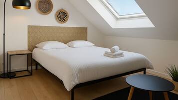 A modern bedroom with a geometric-patterned headboard, a skylight, a bedside table, a round table, and a potted plant.
