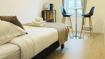 Habitación de hotel con cama, televisión montada en la pared, una mesita con dos sillas y ventana con cortinas.