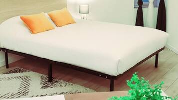 A neatly made bed with two orange pillows, a bedside lamp, and a potted plant on a wooden floor.