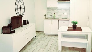 A modern kitchen with white cabinetry, a clock, a television, and a dining area with a plant. - Résidence La Cocarde (Bourges)