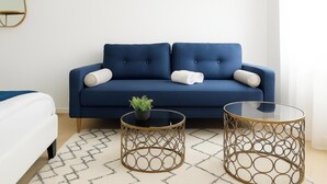 A modern living room with a blue sofa, two round gold tables, and a small potted plant. - Résidence La Cocarde (Bourges)