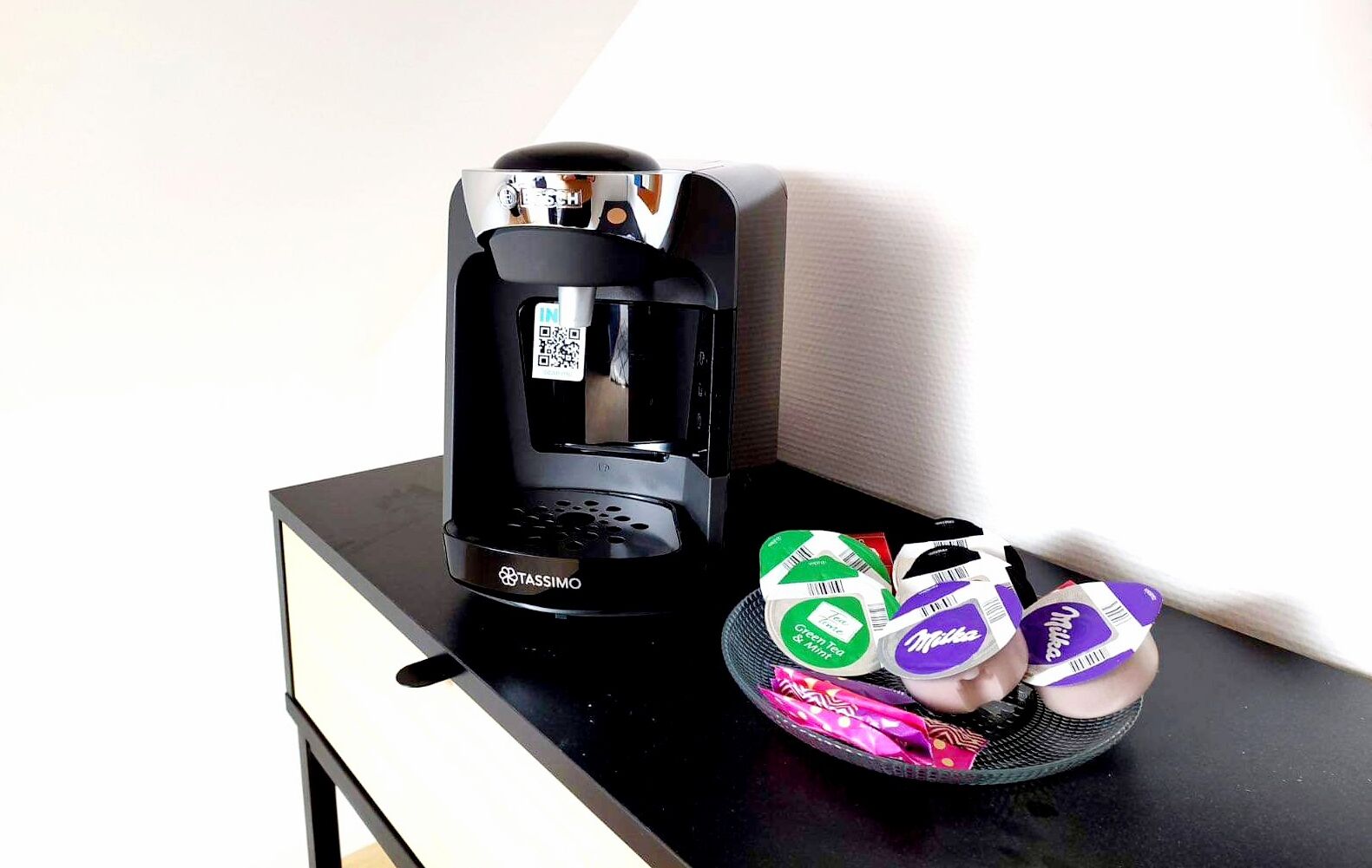 A Tassimo coffee maker on a black countertop with a basket of Tassimo pods.