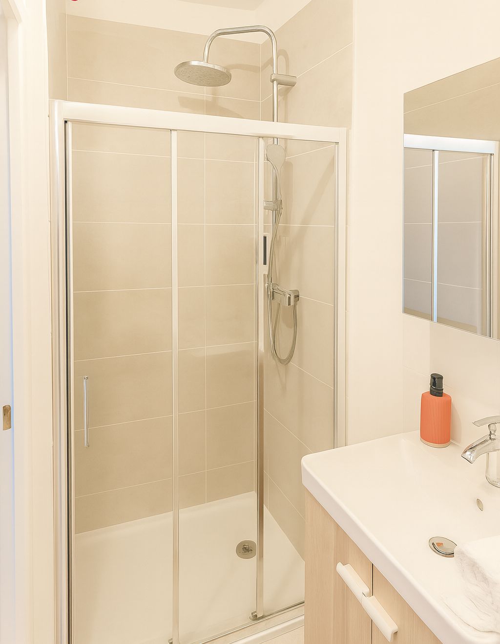 Een moderne badkamer met een douchecabine van glas, een witte wastafel met spiegel en een zeepfles.