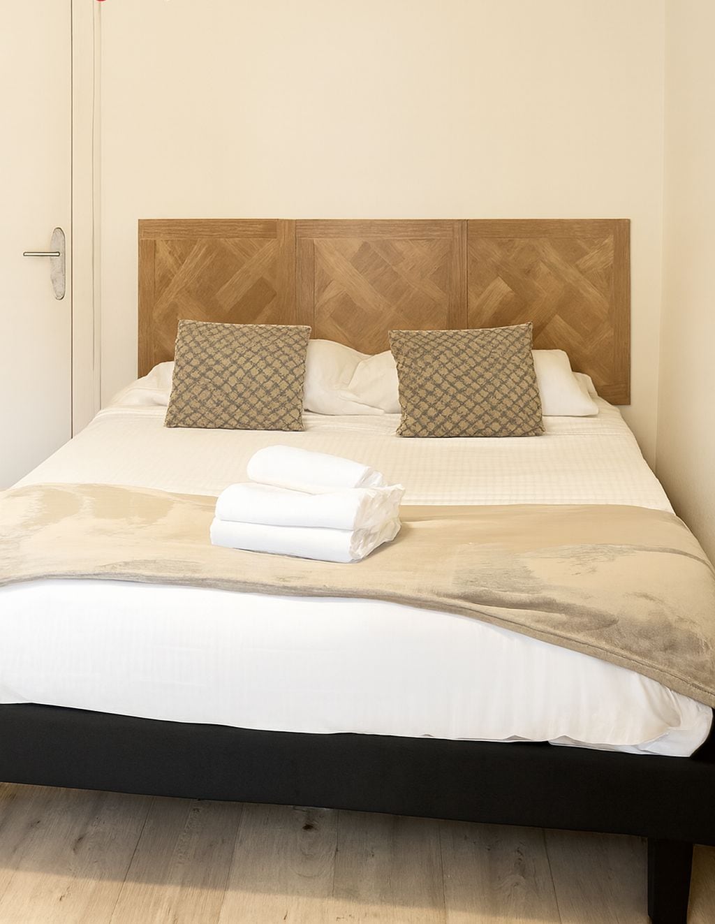 Un lit bien fait, avec une tête de lit en bois, deux coussins à motifs et des serviettes blanches pliées.